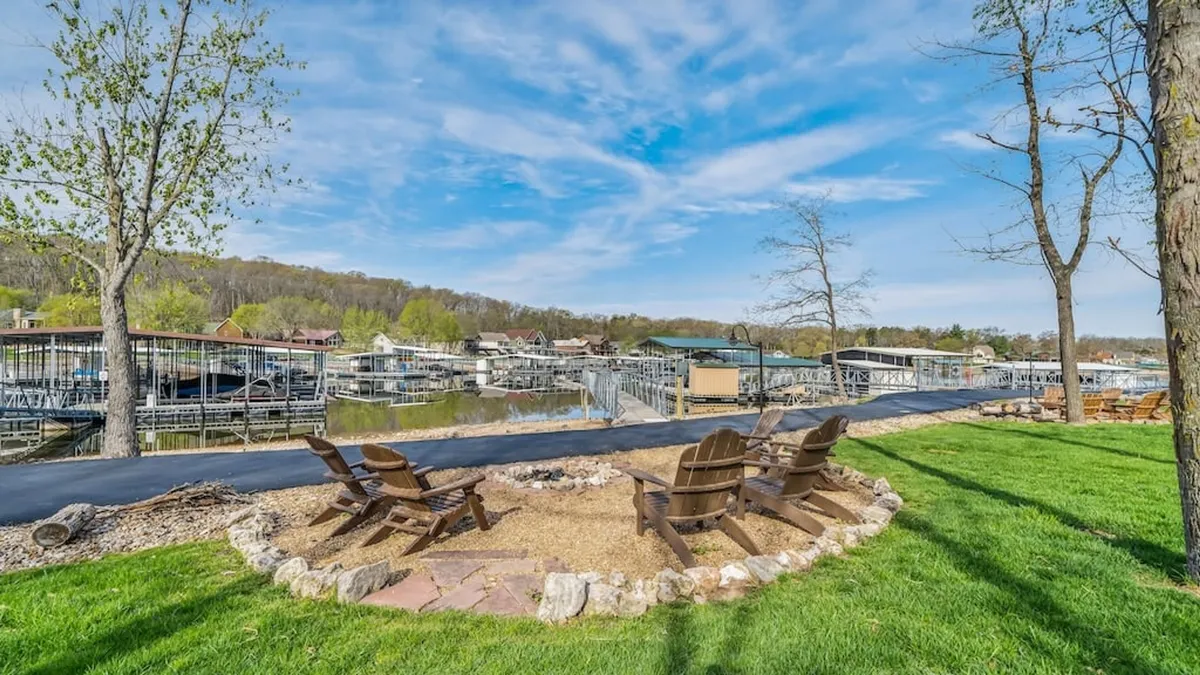A cozy fire pit surrounded by Adirondack chairs sits near the water's edge, with a view of the dock and the lake beyond. The scene is illuminated by the warm glow of sunset, evoking feelings of togetherness and relaxation after a day on the water.