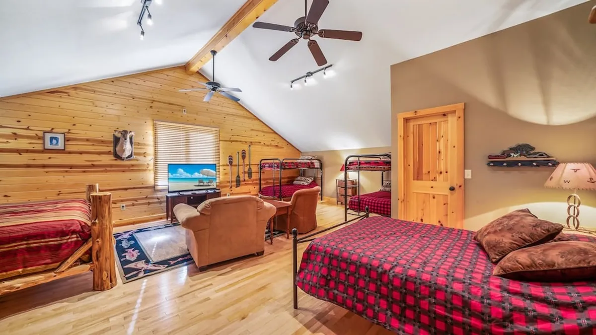 A comfortable downstairs living area with a sofa seating area, television, and built-in bunk beds under a wooden ceiling, creating a space perfect for movie nights, games, and communal relaxation.