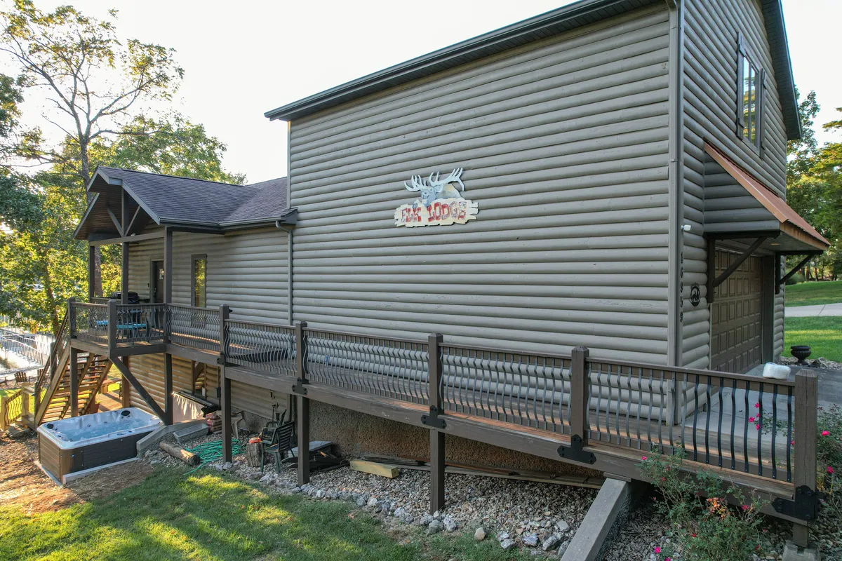 A view of the wooden deck at Elk Lodge, featuring a hot tub, lodge sign, and comfortable seating. The space is oriented for relaxation, with the promise of sunset views and opportunities for stargazing or enjoying coffee in the fresh air.