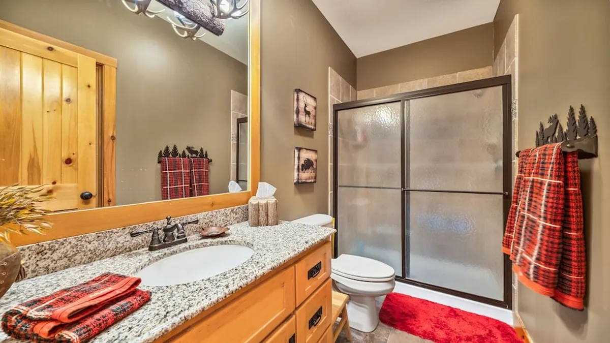 A warmly lit bathroom with granite countertops, wooden cabinetry, a glass shower enclosure, decorative towels, and artwork on the walls. The inviting space promises relaxation and the gentle routine of refreshing showers after an active day.