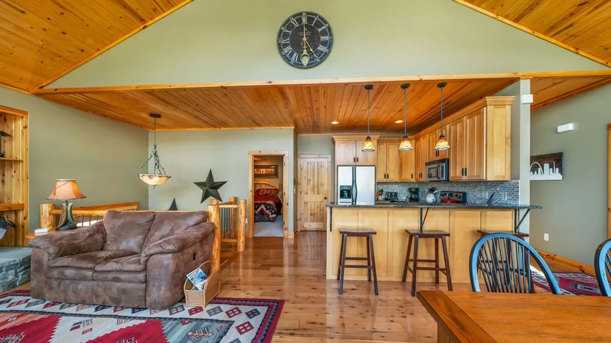 An open main living area with a wooden ceiling, a spacious kitchen island, a comfortable sofa, and a decorative rug. The setup encourages both cooking and socializing, ideal for group gatherings and shared meals.