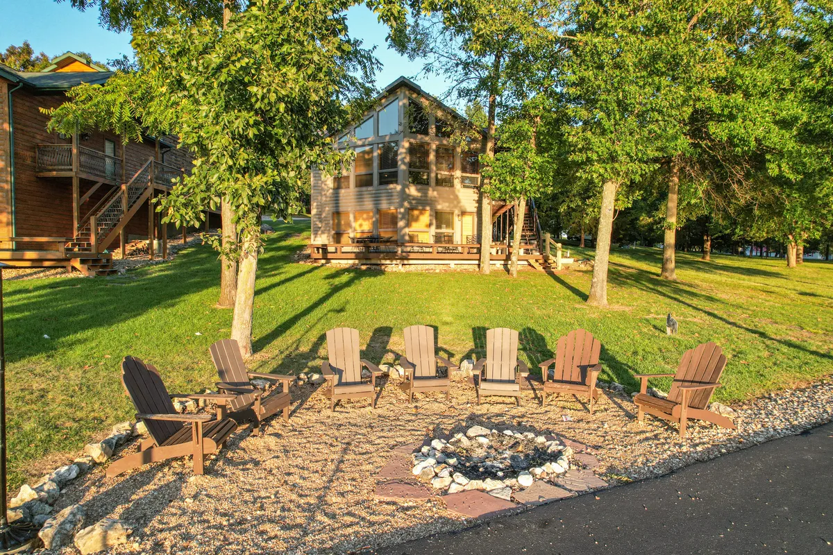 A welcoming fire pit area with Adirondack chairs surrounded by trees, the house visible in the background. The setting is perfect for gathering at day’s end, sharing stories, and enjoying the peaceful lake ambiance.